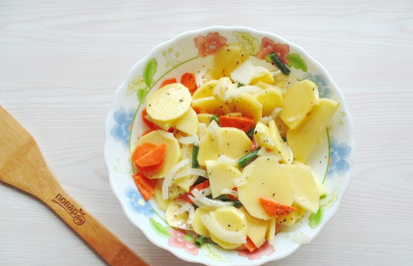 1. Этап. Запеканка с куриными ножками: Картофель вымойте, очистите, ополосните и нарежьте кружками толщиной 2-3 мм. Также переложите в отдельную глубокую миску. Добавьте сюда же стручковую фасоль, нарезанную тонкими кружками морковь и репчатый лук. Посолите, поперчите и добавьте половину чайной ложки базилика. Влейте растительное масло и хорошо перемешайте все ингредиенты.