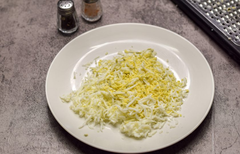 1. Этап. Салат Оля-ля: Куриные яйца сварите вкрутую — 12 минут, после остудите и почистите. Натрите яйца на мелкой терке.