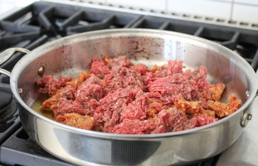 1. Этап. Вкусная лазанья: На сковороде разогрейте масло. Добавьте в него фарш и измельченные сосиски.