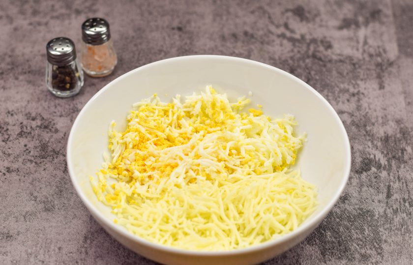 1. Этап. Пикантная закуска на чипсах: Остудите и очистите куриное яйцо, после натрите его на мелкой терке, переложите в тарелку. Также натрите на мелкой терке сыр, добавьте к яйцу.