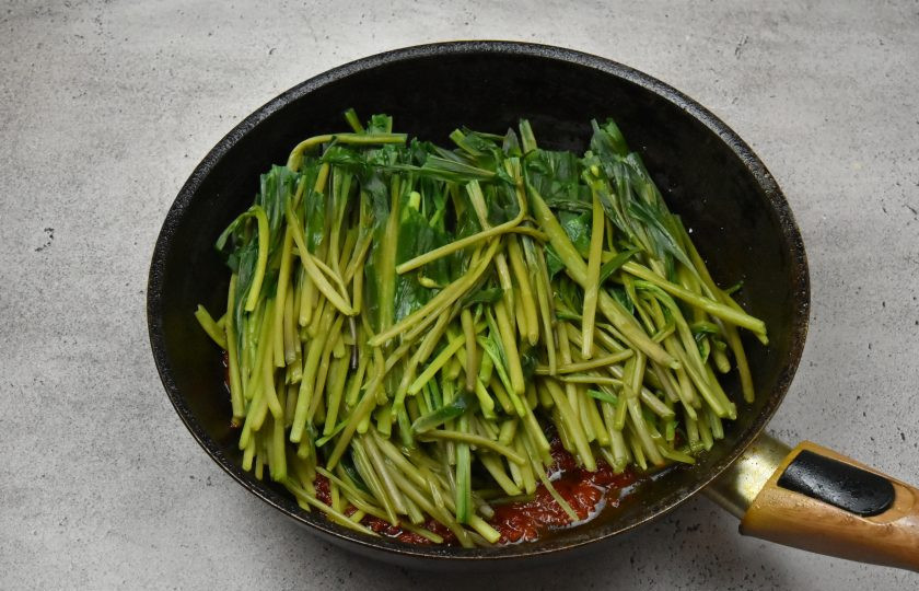 1. Этап. Черемша в томатном соусе на зиму: В сковороду переложите подготовленные стебли черемши, добавьте соль, сахар. Аккуратно перемешайте содержимое. Удобно воспользоваться кулинарными щипцами.