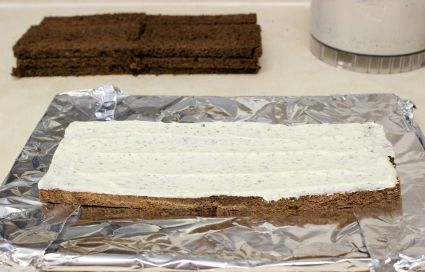 1. Этап. Торт с копченым лососем: Ржаной хлеб избавьте от корок и нарежьте на кусочки, толщина ломтика не должна быть более 4–5 мм. Обверните тарелку фольгой, выложите первый слой и смажьте его сливочным сыром.