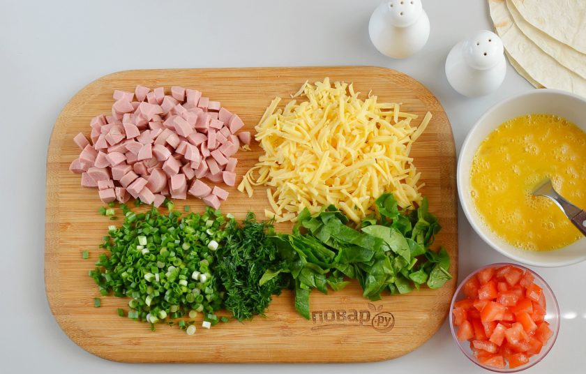 1. Этап. Завтрак с лавашом: Взболтайте три яйца с солью и перцем. Натрите сыр на терке, порежьте кубиками сосиски, порежьте зелень. Помидор разрежьте на 4 части, удалите семена, а плотные части порежьте кубиками.