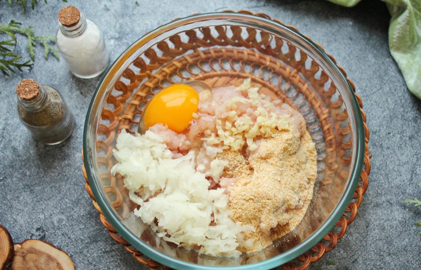 1. Этап. Куриные биточки в духовке с подливкой: В миску выложите куриный фарш, вбейте яйцо и всыпьте панировочные сухари. Репчатый лук и чеснок почистите и натрите на крупной терке, добавьте к фаршу.