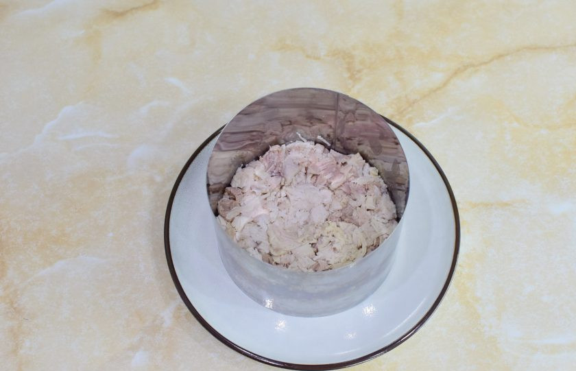 1. Этап. Салат с курицей, сыром и маринованными грибами: Для формовки салата будем использовать сервировочное кольцо. Поставьте его на тарелку и выложите первым слоем нарезанную курицу. Немного смажьте майонезом.