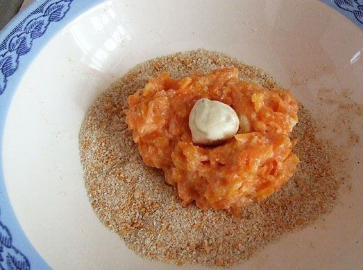 1. Этап. Котлеты из моркови: Насыпаем в глубокую миску панировочные сухари, выкладываем на них 1-1,5 ложки морковного фарша, а в середину фарша небольшой кусочек плавленого сыра.