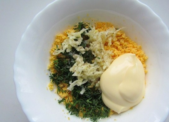 1. Этап. Фаршированные яйца со шпротами и красной икрой: 4. К желтку добавляю чеснок и зелень, по вкусу солю и перчу, кладу майонез, перемешиваю.