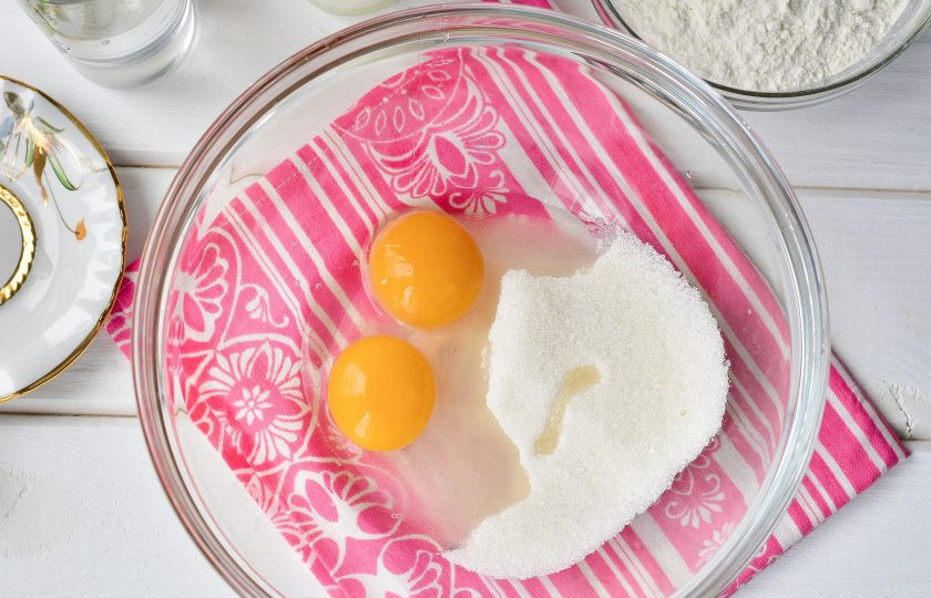 1. Этап. Оладьи на кефире с кипятком: Вбейте в миску яйца и добавьте к ним сахар.