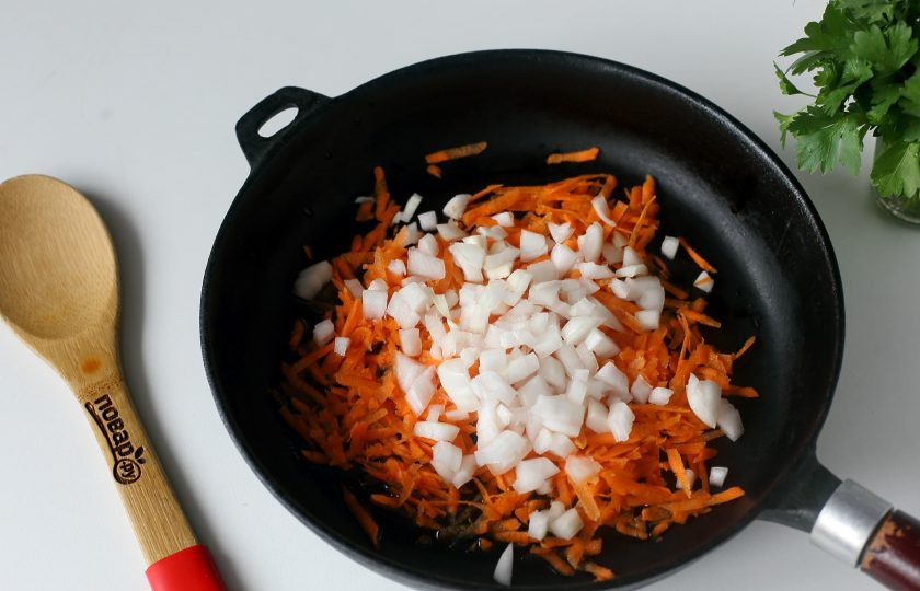 1. Этап. Суп с гречкой и фасолью: Лук нарежьте кубиками, а морковь натрите на терке. Выложите овощи на разогретую сковороду с маслом.