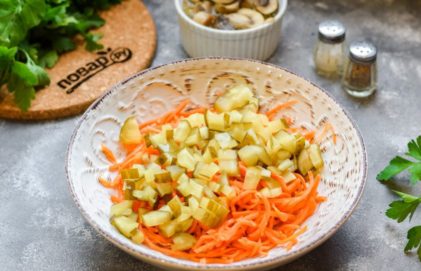 1. Этап. Салат с курицей и маринованными шампиньонами: Квашеные огурцы нарежьте небольшими кубиками и добавьте в емкость к моркови.