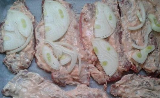 1. Этап. Свинина по-гусарски: Застилаем противень пергаментом и выкладываем не него свинину. Репчатый лук нарезаем полукольцами и кладем на мясо.