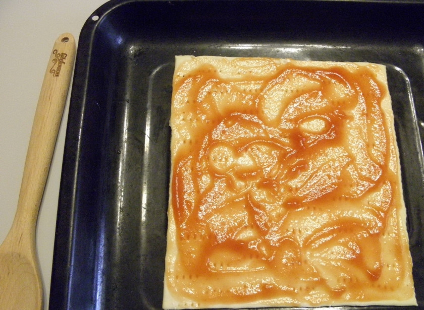 1. Этап. Пицца из слоеного теста в духовке: Переложите тесто на противень. Обязательно сделайте проколы вилкой в нескольких местах, чтобы тесто не вздувалось. Смажьте томатным соусом.