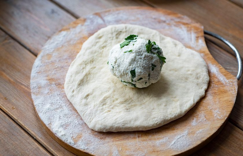 1. Этап. Хычины с творогом: Припылите рабочую поверхность мукой и одну часть теста раскатайте в лепешку. На центр лепешки выложите одну часть начинки.