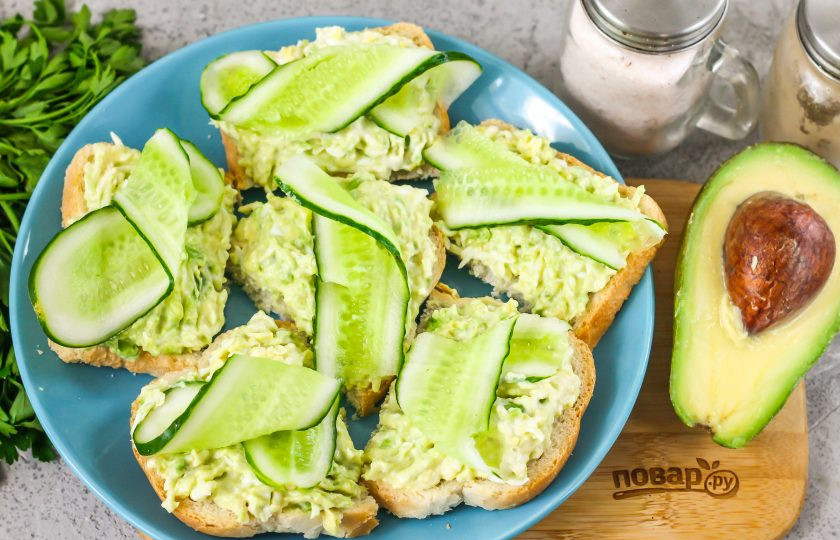 1. Этап. Бутерброды с авокадо и яйцом: Промойте свежий огурец в воде, срежьте с овоща хвостики. Нарежьте его лентами и украсьте бутерброды. По желанию можно добавить и свежую зелень.