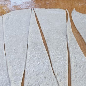 1. Этап. Булочки с сыром: Подошедшее тесто делим на две части и раскатываем каждую в тонкий прямоугольный пласт и смазываем мягким сливочным маслом. Нарезаем тесто на треугольники. У меня из одного пласта получается 8 треугольников.