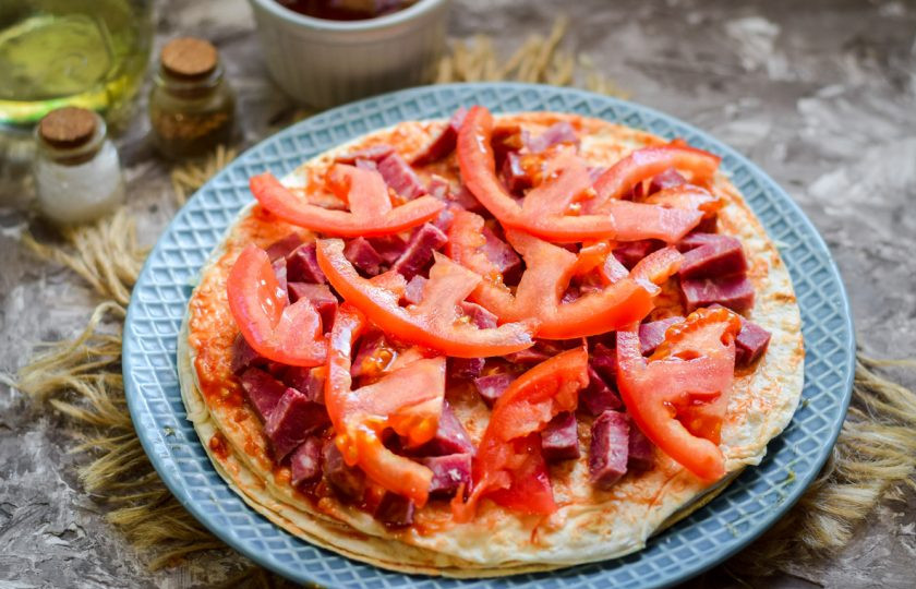 1. Этап. Пицца на сковороде за 15 минут: Помидоры нарежьте небольшими пластинами, выложите поверх колбасы.