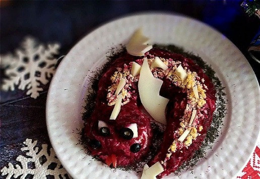 1. Этап. Почти Шуба: Шестой слой и последний - натёртая свёкла. Ею нужно обложить полностью туловище дракончика (сверху и с боков). На голове нужно сделать возвышение, сформировать нос. Салфеткой промокните свекольный сок вокруг дракончика на тарелке, чтобы не смотрелось неряшливо. Теперь оформляем дракончика. Для постного салата сыр и яйцо исключите. Замените на огурец например. Я буду использовать твёрдый сыр. Нарезаем несколько треугольников (сколько поместится), вырезаем крылья. По спине присыплем натёртым желтком и вставим треугольники, разместим крылья и на конец хвоста разместим пластинку сыра в виде стрелы.. Для глаз из белка яичного вырежем подходящую фигурку глаза, чтобы разместить на мордочке. У маслин срезаем кружкИ. Крепим их на белок, капнув капельку майонеза. Делаем так же из маслин ноздри. Рот формируем ложкой и вставляем туда 2 маленькие пластинки перца - раздвоенный язык. Вы можете оформить дракончика в своём вкусе. Укроп мелко порубить и присыпать им вокруг фигурки. Дракончик готов, а так же - почти 