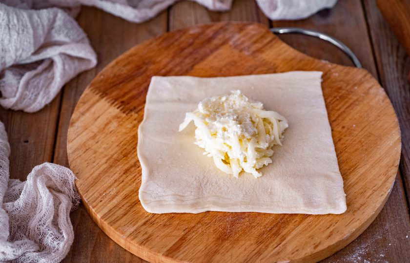 1. Этап. Хачапури из слоеного теста с сыром и творогом: Каждый такой квадрат теста раскатайте немного скалкой. На центр квадрата выложите примерно 2 ст.л. сырно-творожной начинки.