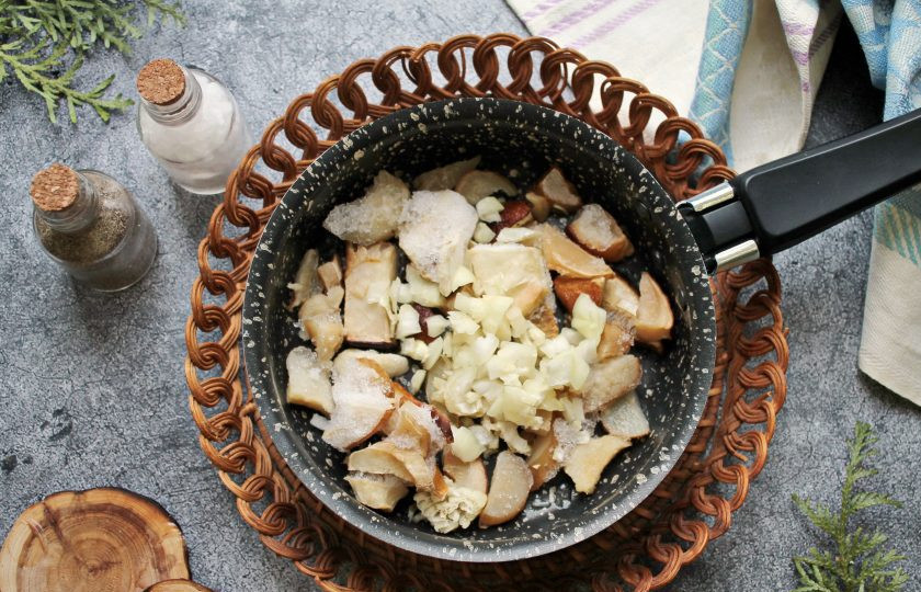 1. Этап. Медальоны с грибами: В сковороду налейте растительное масло и выложите мелко нарезанный репчатый лук. Добавьте нарезанные грибы, не размораживая, и обжаривайте в течение 7 минут на среднем огне, перемешивая.