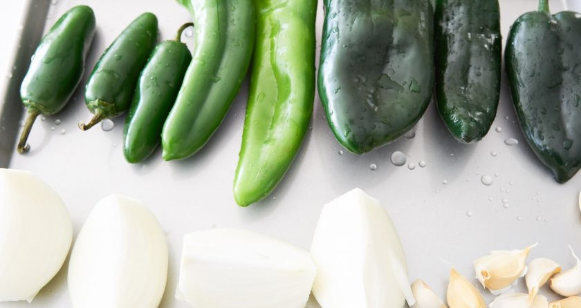 1. Этап. Свинина в зеленом соусе: 1. Помойте перцы и сделайте в них надрезы. Почистите лук и разрежьте его на 4 части. Возьмите чеснок, разделите его на зубчики, но не очищайте от шелухи. Выложите эти ингредиенты на емкость для запекания и поставьте в заранее разогретую до максимума духовку.