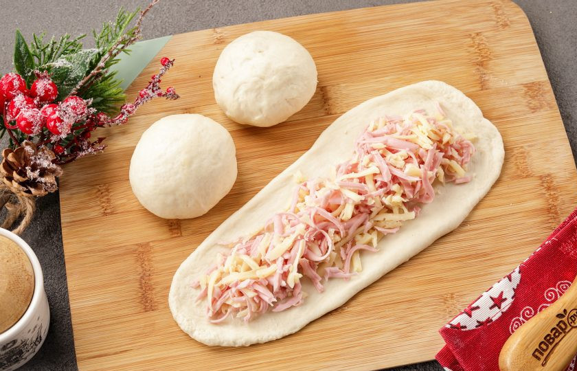 1. Этап. Новогодние пирожки Змейки: Каждую часть теста раскатайте как на фото, чтобы одна сторона была чуть шире другой и выложите по центру начинку. Защипните края, смажьте руки растительным маслом и слега потяните заготовку руками, чтобы она стала чуть длиннее.