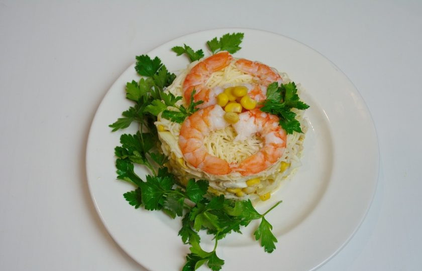 1. Этап. Салат 8 Марта с кальмарами: Из креветок или колец кальмара изобразите восьмерку на салате. Края украсьте зеленью. Место соединения украсьте кукурузными зернами