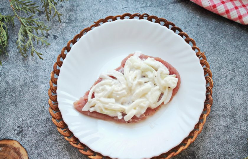 1. Этап. Мясо по-французски со свининой: Репчатый лук смешайте с майонезом и разложите по отбитым кускам свинины.