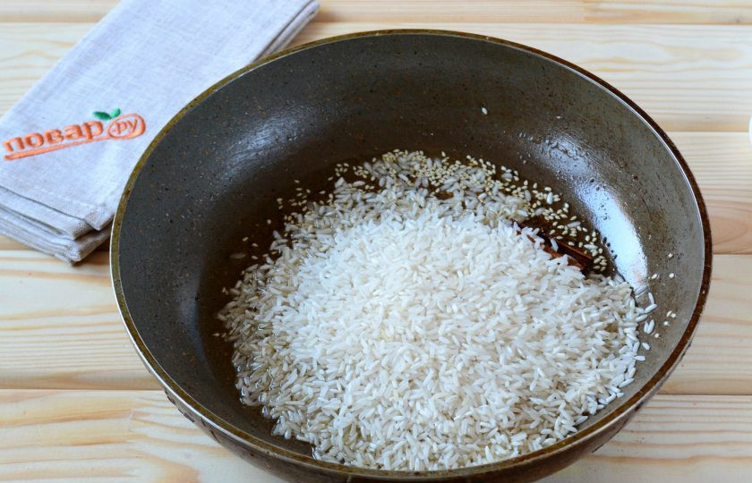 1. Этап. Гаджар Пулау: В большой сковороде разогрейте растительное масло, отправьте туда все подготовленные специи, корицу и кунжут. Слегка обжарьте и добавьте рис. Готовьте несколько минут на среднем огне, пока рис не получит красивый золотистый оттенок.