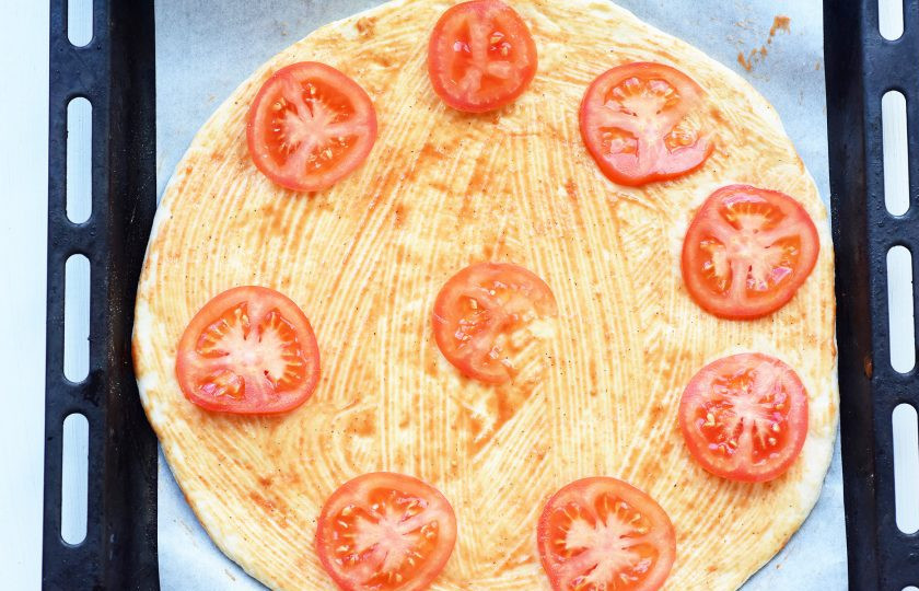 1. Этап. Пицца на сухом молоке: Раскатайте тесто в пласт круглой формы (диаметр примерно 34-36 см.), выложите на противень, застеленный пергаментом для выпекания, смажьте тонким слоем томатного соуса, разложите кружочки помидоров.