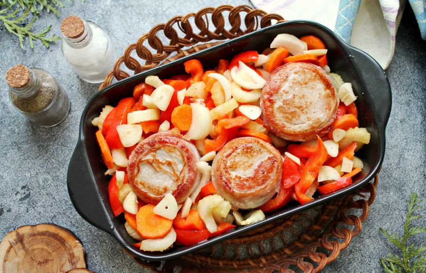 1. Этап. Свиные медальоны в беконе запеченные с овощами: Форму с овощами достаньте из духовки, уберите фольгу и выложите свиные медальоны, сняв полоски. Выложите наверх каждого медальона по маленькому кусочку сливочного масла и запекайте еще 25 минут. Готовые свиные медальоны в беконе с овощами достаньте из духовки и сразу подавайте к столу.