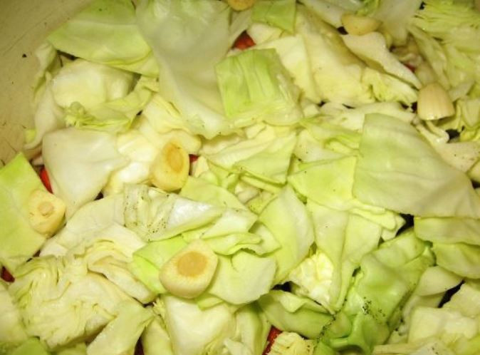1. Этап. Дамлама из баранины: Отложите несколько листьев капусты, остальную порежьте и отправьте в кастрюлю. Сверху кружки баклажана и половину крупно нарезанного чеснока.