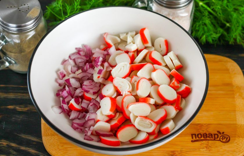 1. Этап. Салат с сыром косичка и крабовыми палочками: Очистите от кожуры красный лук, промойте его в воде. Размороженные крабовые палочки нарежьте кружочками. Луковицу нарежьте мелким кубиком и высыпьте обе нарезки в салатник или миску.