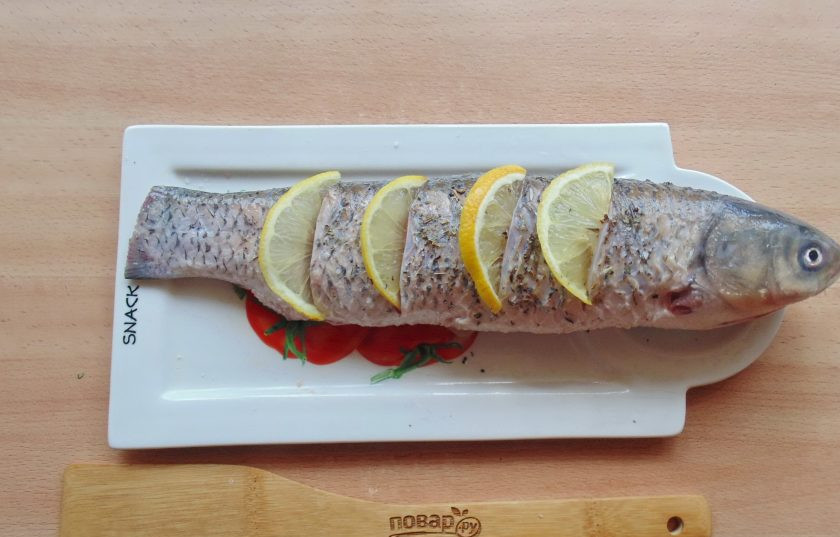 1. Этап. Белый амур в фольге в духовке: Сделайте на тушке рыбы небольшие надрезы и вставьте ломтики лимона.