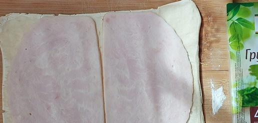 1. Этап. Слойки с ветчиной, изюмом и оливками: Тесто, слегка присыпав мукой, раскатать в длину. Уложить ветчину.