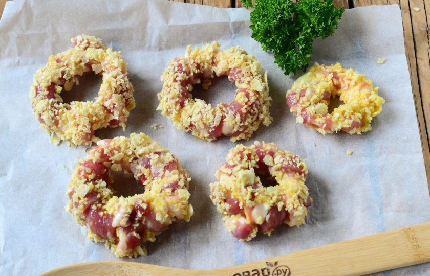 1. Этап. Луковые кольца в беконе и панировке: Выложите луковые кольца в панировке на противень, застеленный пергаментом. Отправьте в духовку на 20-25 минут (температура — 180 градусов).