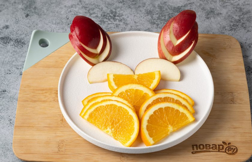 1. Этап. Фруктовая нарезка Дракон на Новый год: Добавьте на тарелку уши дракона из яблок и глаза.