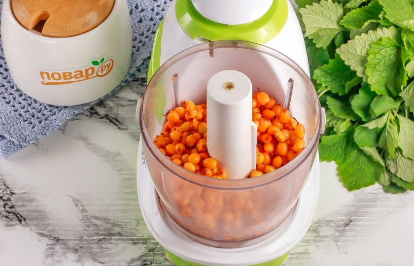 1. Этап. Облепиха без сахара на зиму: Обсушите облепиху бумажными салфетками, минимизируя лишнюю влагу. Затем пересыпьте половину ягод в чашу измельчителя или кухонного комбайна. Погружным блендером не пользуйтесь, так как он перебьет и косточки.