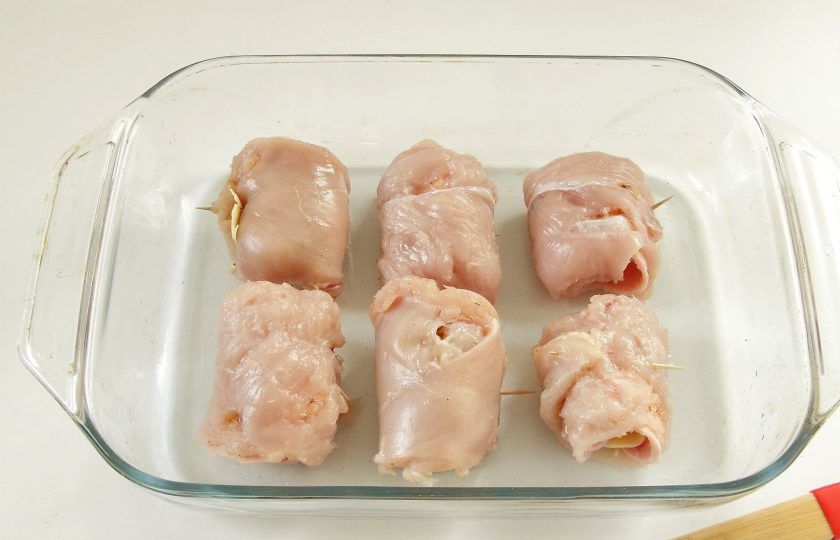 1. Этап. Куриные роллы с ветчиной и сыром: 5. Аккуратно сверните каждое филе с начинкой рулетиком и закрепите края зубочисткой. Выложите готовые роллы в форму для запекания, смазанную маслом.