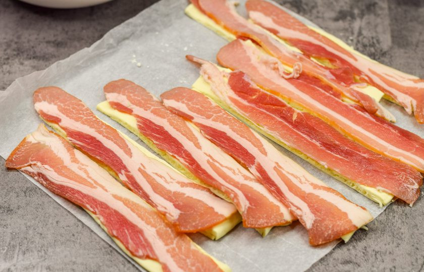 1. Этап. Слоеные палочки с сыром и беконом: На каждую заготовку теста выложите полоску бекона.