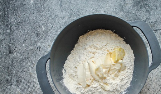 1. Этап. Закусочное печенье с ветчиной и сыром: Муку просейте в миску, добавьте сливочное масло, посолите и перетрите в мучную крошку. Для удобства масло можно натереть на крупной терке или порезать мелким кубиком.