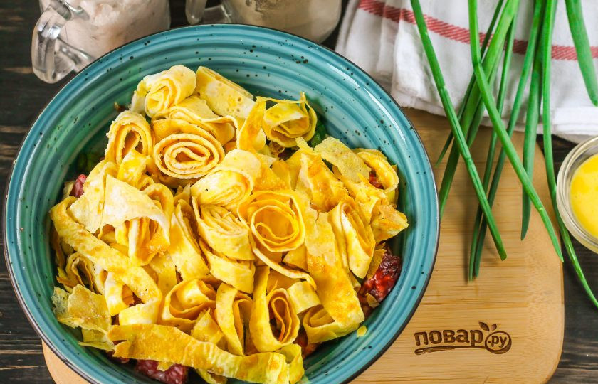 1. Этап. Салат с яичными блинчиками и луком: Сверните остывшие яичные блинчики рулетиком и нарежьте, добавьте в емкость.