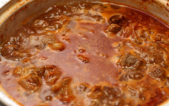 1. Этап. Гуляш из свинины с помидорами: Наливаем в к мясу с луком воду. Воды должно быть столько, чтобы она полностью покрывала мясо. Доводим гуляш до кипения, накрываем крышкой и уменьшаем огонь под сковородкой до минимального. Готовим до мягкости мяса.