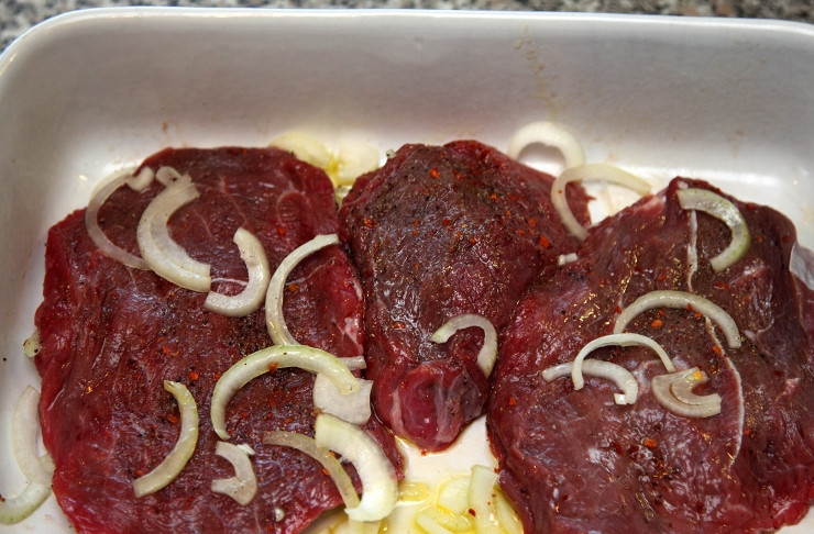 1. Этап. Маринованная говядина: Выкладываем кусочки мяса в широкую форму, посыпаем их подготовленными специями, солим по вкусу, добавляем репчатый лук и немного оливкового масла.