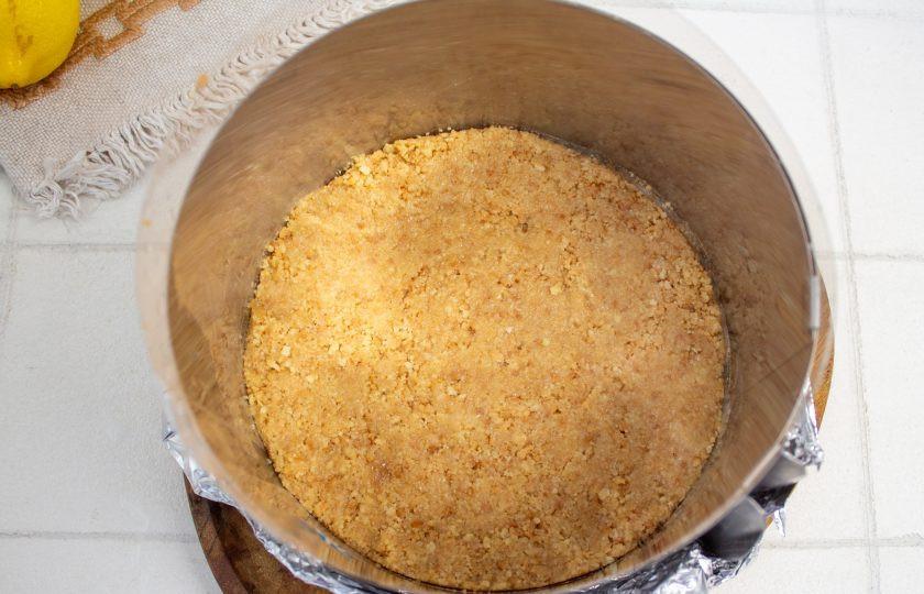 1. Этап. Лимонный чизкейк без выпечки: Форму для выпечки диаметром 16 см. выстелите ацетатной пленкой, а дно оберните в несколько слоев фольги. Выложите основу из печенья и плотно ее утрамбуйте.