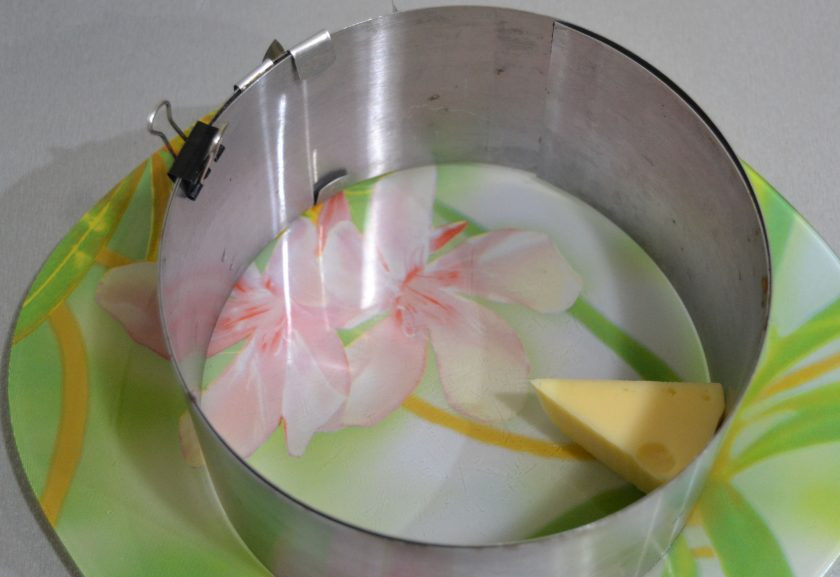 1. Этап. Салат Мышки-шалунишки: Салат лучше собирать с помощью сервировочного кольца, положите внутрь кусок сыра треугольной формы, лучше обернуть этот кусок сыра пищевой пленкой, так как его потом следует извлечь.