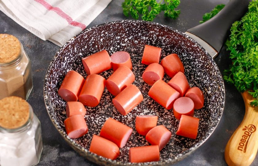 1. Этап. Сосиски по-корейски: Сосиски очистите от оболочки и нарежьте порционными кусочками. Прогрейте в сковороде растительное масло и выложите в него кусочки сосисок. Нагрев убавьте до минимального. Обжарьте сосиски примерно 2-3 минуты.