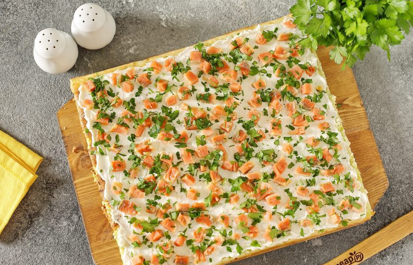 1. Этап. Рулет из кабачков с семгой и сыром: Готовый корж вместе с пергаментом или ковриком переложите на решетку для остывания, когда корж немного остынет, переложите его на ровную поверхность, смажьте сыром, посыпьте измельченной кусочками семгой и рубленой зеленью.