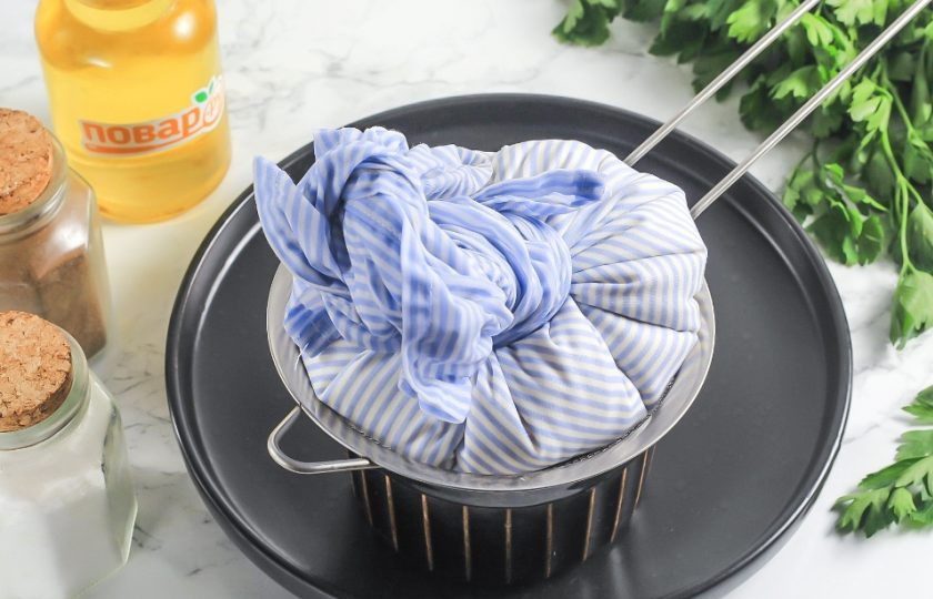 1. Этап. Домашняя брынза из творога: Застелите ситечко двойным слоем марли или льняной, хлопчатобумажной салфеткой. Перелейте содержимое емкости на ситечко. Сыворотка сольется в емкость под ситечком, а творог останется в марле. Соберите ткань за края и подвесьте в виде колобка над раковиной на 15-20 минут, чтобы слить лишнюю жидкость.