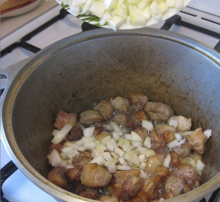 1. Этап. Лагман из свинины: 2. Вымыть, просушить и нарезать небольшими кусочками мясо. В кастрюлю с толстым дном или сотейник налить масла и хорошо его разогреть. Отправить туда мясо и обжарить до золотистой корочки. Затем отправить к мясу лук.