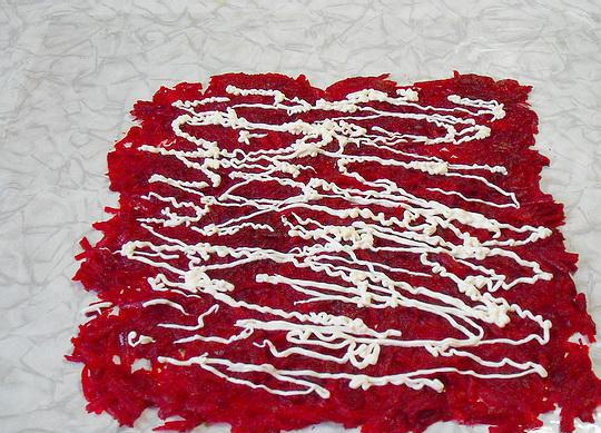 1. Этап. Рулет с сельдью на Старый Новый год: 4. На столе расстилаем пищевую пленку, растительным маслом ее смазываем и на пленку выкладываем слой свеклы в форме квадрата. Наносим сверху майонезную сеточку. Следующий слой выкладываем размером чуть меньше предыдущего. Вторым слоем будет морковь, потом сеточка из майонеза, после – картофельный слой, и снова майонез.